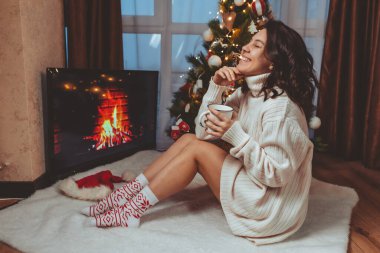 Lviv, Ukrayna - 15 Aralık 2021: Genç güzel bir kadın noel ağacının yanında oturmuş kahve içiyor fotokopi uzayı