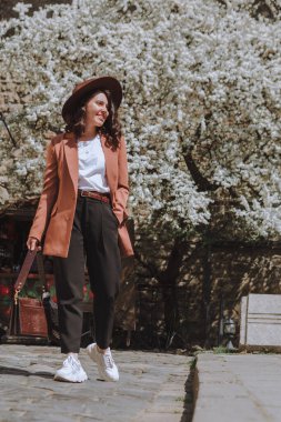 Gülümseyen, ceketli ve şapkalı güzel bir kadın. Arka planda, Spring City Caddesi 'nde yürüyen beyaz çiçek açan bir ağaç.