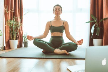 Kadın bilgisayarın yanında yoga yapıyor çevrimiçi öğrenim uzaktan spor eğitimi veriyor.