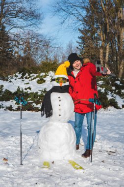 Kayakçı kardan adamla selfie çeken bir adam.