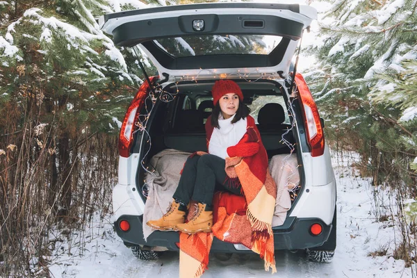 Mujer bonita sonriente en el maletero del coche en el bosque de invierno nevado — Foto de Stock