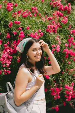 Genç, güzel, gülümseyen bir kadın, kırmızı güllerin yanında.