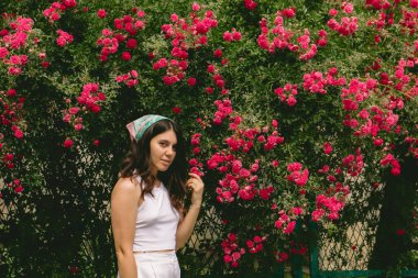 Genç, güzel, gülümseyen bir kadın, kırmızı güllerin yanında.