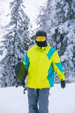 Snowboard 'lu bir adam karlı tepenin yanından geçiyor.
