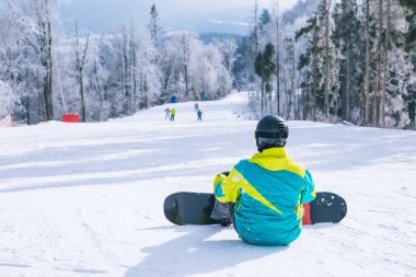Tepede oturan adam manzaranın tadını çıkarıyor. Snowboard. Kış sporları. Boşluğu kopyala