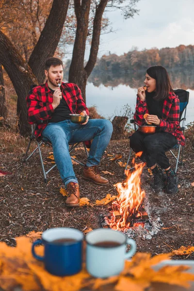 smiling happy couple resting near fire cooking food autumn camping concept