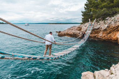 Asma köprüden yürüyen adam yaz mevsiminde kayalık körfezi geçiyor.