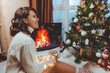 Lviv, Ukrayna - 15 Aralık 2021: Genç güzel bir kadın noel ağacının yanında oturmuş kahve içiyor fotokopi uzayı