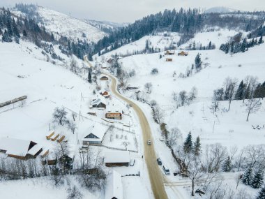 Karpatya dağlarının ortasındaki karlı köydeki hava manzaralı yol Ukrayna 'ya çıkıyor.