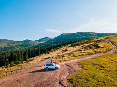 aerial view of couple sitting on the suv car roof enjoying view of carpathian mountains Ukraine clipart