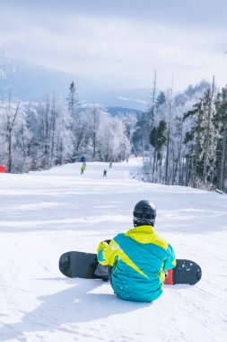 Tepede oturan adam manzaranın tadını çıkarıyor. Snowboard. Kış sporları. Boşluğu kopyala