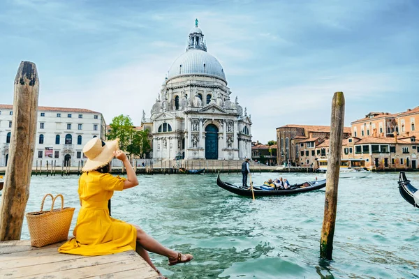 Sarı elbiseli kadın, İtalya yaz tatilinde Venedik Kanalı manzaralı iskelede oturuyor. Boşluğu kopyala