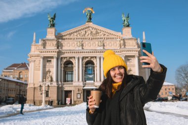 Kadın gezgin, opera binası Ukrayna 'nın önünde selfie çekmek için kahve içiyor.