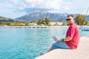 Yazın liman bankında dizüstü bilgisayarda çalışan serbest çalışan bir adam.