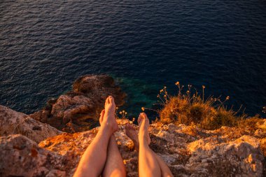 Uçurumda oturan çift gün batımının tadını çıkarıyor.