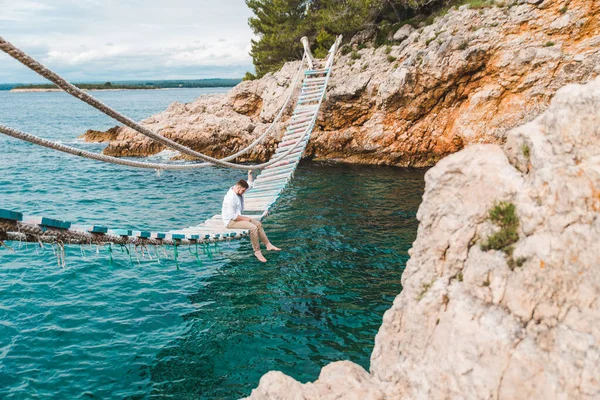Man zittend op hangbrug genieten van uitzicht op zee en de natuur rust — Stockfoto