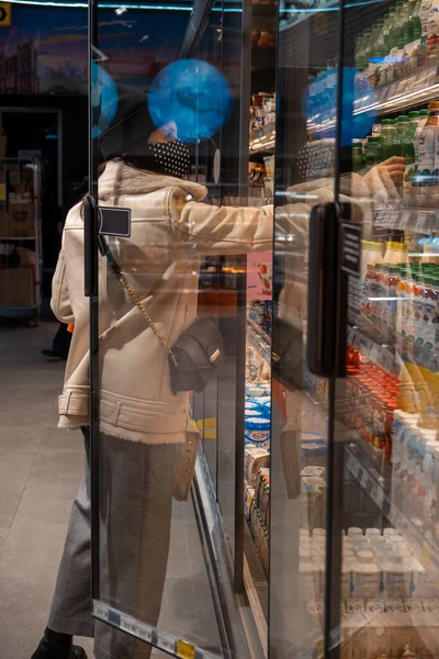 Kobieta Płaszczu Masce Medycznej Sklepie Spożywczym Otwierając Drzwi Lodówki — Zdjęcie stockowe