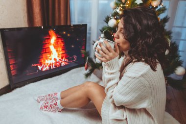 Lviv, Ukrayna - 15 Aralık 2021: Genç güzel bir kadın noel ağacının yanında oturmuş kahve içiyor fotokopi uzayı