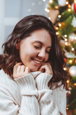 Beyaz kazaklı kadın Noel ağacı portresinin yanında poz veriyor.