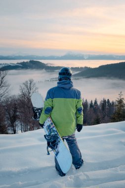 Snowboard yapan adam, kar dağlarının tepesindeki kış yolculuğunun tadını çıkarıyor.