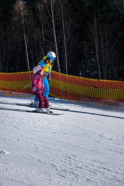 Kayak pistinde genç bir aile kızına kayak öğretiyor.