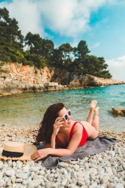 Kadın deniz sahilinde battaniyeye uzanmış fotokopi çekiyordu.