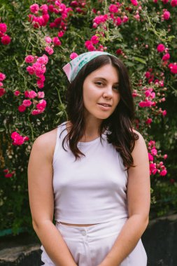 Genç, güzel, gülümseyen bir kadın, kırmızı güllerin yanında.