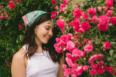 Genç, güzel, gülümseyen bir kadın, kırmızı güllerin yanında.