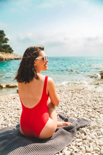 Deniz kıyısı yaz tatilinde battaniyeye oturmuş bir kadın.