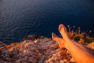 Kadın bacakları gün batımında uçurumda deniz tatili