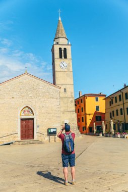 Hırvatistan 'da Fazana' da çan kulesiyle kilisenin fotoğrafını çeken bir adam. yaz tatili