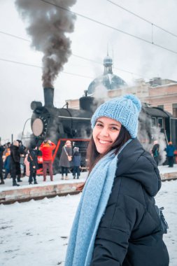 Tren istasyonunda gülümseyen kadın portresi. Eski buharlı trenin yanında kış zamanı.