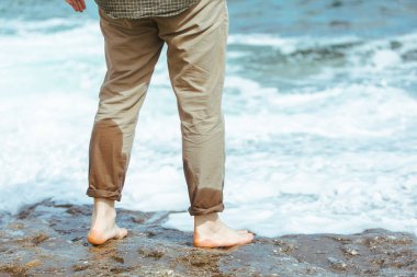 Deniz kıyısında yürürken pantolonlu ıslak adam bacakları suyun tadını çıkarıyor. yaz tatili