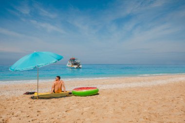 Deniz kıyısında güneşli bir günde güneşli bir şemsiye Yunan tatil gezisi arka planda küçük bir tekne.