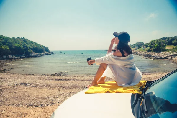 女人坐在车篷边喝咖啡 欣赏夏日的海景 — 图库照片