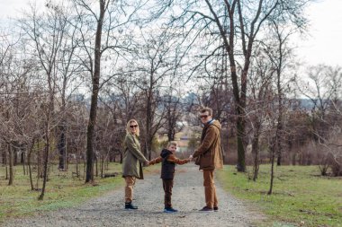 Genç, mutlu bir aile babası, anne ve oğlu. Arkadan bak. Şehir parkının yanından geçiyor.