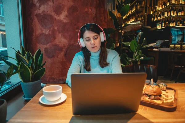 Woman freelancer working on laptop in cafe drinking tea eating burger — Stock Photo, Image