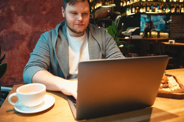 Man freelancer working on laptop in cafe eating burger and drinking tea — Stock Photo, Image
