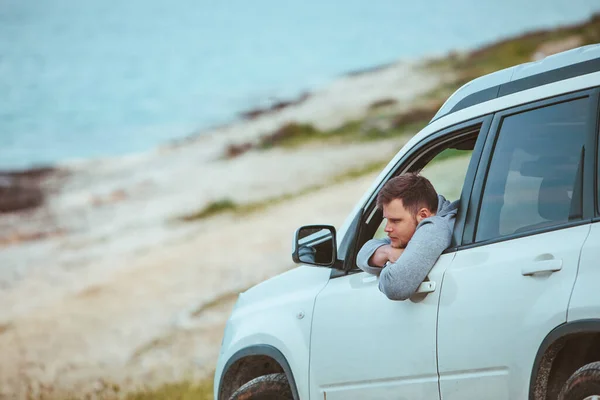 smiling man stick out from car window. summer sea on background. copy space. rent car travel concept