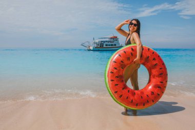 Mutlu, gülümseyen bir kadın, arka planda Yunan tatilinde şişme yüzük taşıyan küçük bir yolcu gemisi.