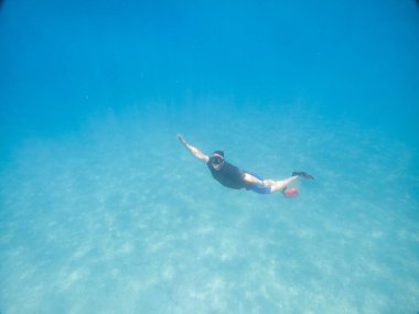 Skuba maskeli bir adam yaz tatilinde suyun altında fotoğraf çekiyor.