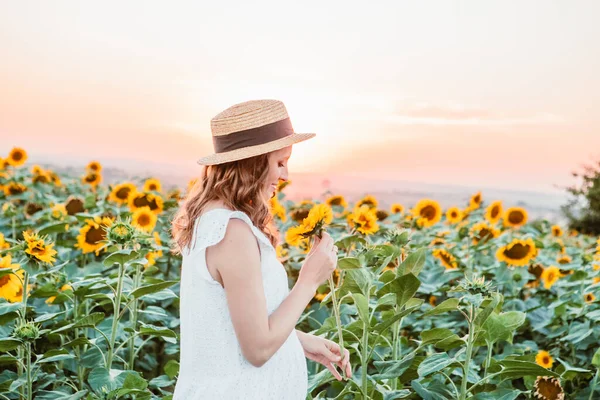 young pretty woman in white sundress at blooming sunflowers field
