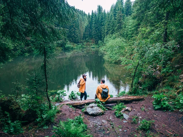 穿着黄色雨衣的徒步旅行者看着高山湖中的背包客 — 图库照片