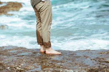 Deniz kıyısında yürürken pantolonlu ıslak adam bacakları suyun tadını çıkarıyor. yaz tatili