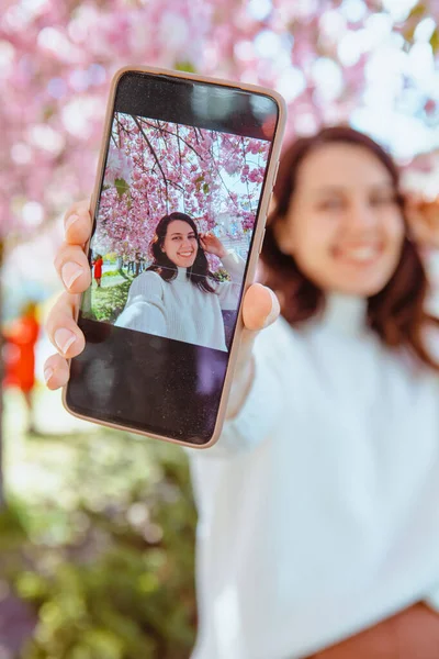 Woman shooting her self on the phone under blooming sakura tree — Stock Photo, Image