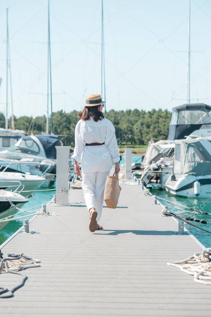 young pretty woman in white summer clothing walking by yachts dock. copy space