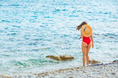 Yaz tatili için deniz kenarında hasır şapkalı genç ve güzel bir kadın. Kırmızı mayo.