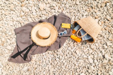 Plaj malzemesi battaniyesi, güneş koruması, krem hasır şapka ve düz çanta.