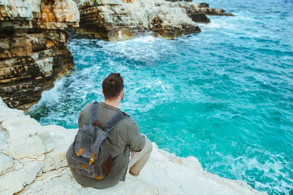 sırt çantası ile adam şehir manzarası zevk uçurumun üzerinde oturan. yaz tatili
