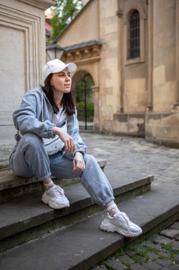 Güzel, gülümseyen bir kadın açık havada bol spor giysiler içinde poz veriyor.